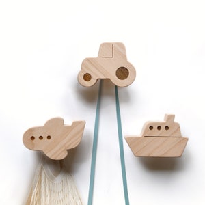 May include: Three wooden wall hooks shaped like a tractor, airplane, and boat. Each hook has a light blue ribbon attached.