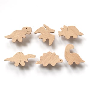 May include: Six wooden dinosaur toys in various shapes and sizes, including a T-Rex, Stegosaurus, Triceratops, and Pterodactyl. The toys are all made of natural wood and have a light brown color.
