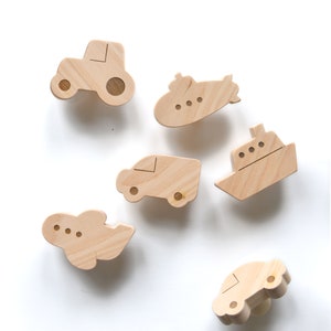 Peut inclure: Ensemble de six crochets muraux en bois en forme de différents véhicules, dont un tracteur, un sous-marin, une voiture, un avion et deux bateaux. Les crochets sont en bois naturel et ont une couleur brun clair.