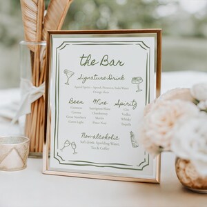 May include: A rectangular bar menu sign in a thin metallic frame with olive green text and line art illustrations. The menu lists sections for the Bar, Signature Drink, Beer, Wine, Spirits, and Non-alcoholic options with various drink names.