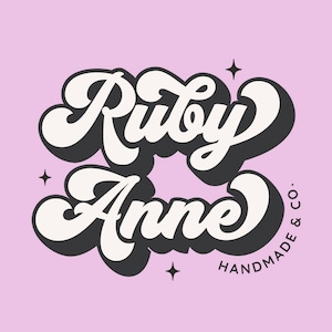 May include: A white and black logo with the text "Ruby Anne" in a retro, cursive font. The text "HANDMADE & CO." is written in a smaller font below the main text.