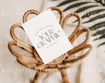 Può includere: Un mockup di carta bianca con il testo "SMART OBJECT MOCKUP YOUR GRAPHIC ANY CARD MOCKUP" su una sedia in rattan intrecciato.