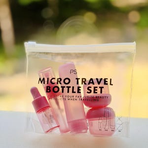 Puede incluir: Un neceser transparente con un juego de micro botellas rosas. El juego incluye pequeños frascos y botes rosas para productos de belleza. El texto "MICRO TRAVEL BOTTLE SET" está impreso en el neceser.