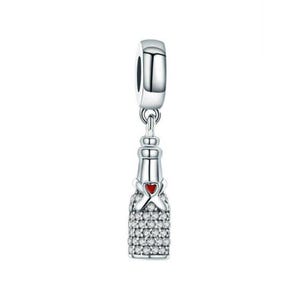 Puede incluir: Un dije plateado con forma de botella de champán, que presenta un cuello liso y un cuerpo incrustado con numerosas piedras pequeñas, claras y brillantes. Un pequeño detalle de corazón rojo vibrante se sitúa en el centro del cuello de la botella.