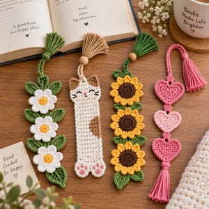 Puede incluir: Cuatro marcapáginas de ganchillo hechos a mano con diseños distintos: una enredadera verde con tres flores blancas, un gato crema y marrón con almohadillas rosas, una enredadera verde con tres girasoles amarillos y tres corazones rosas con borla.