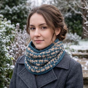 Peut inclure: Un col en crochet bleu sarcelle et beige présentant un motif géométrique répétitif et texturé. L'accessoire est porté autour du cou, mettant en valeur une construction épaisse et bouclée avec un bord côtelé sur un manteau gris foncé.