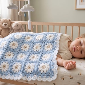 Può includere: Una coperta per neonati lavorata all'uncinetto a mano con un motivo quadrato ripetuto di margherite bianche con centri beige su sfondo azzurro, rifinita con un bordo bianco smerlato che copre un bambino che dorme in una culla di legno.