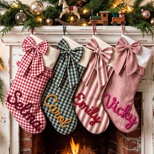 May include: Four personalized Christmas stockings hanging in a row. The first is red and white gingham with the name Selma, the second is green and white plaid with the name Carol, the third is red and white striped with the name Emily, and the fourth is solid dusty pink with the name Vicky. Each stocking features a large fabric bow at the top.