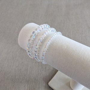 K&ouml;nnte beinhalten: Drei irisierende wei&szlig;e Perlenarmb&auml;nder, die auf einem wei&szlig;en Pr&auml;sentationsst&auml;nder gestapelt sind.