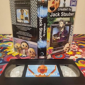 May include: A VHS tape and case featuring artwork and text from "created by Jack Stauber." The tape has the words "HAVE MY DIRT" on it. The case has various illustrations and the text "as seen on [as]" and "created by Jack Stauber."