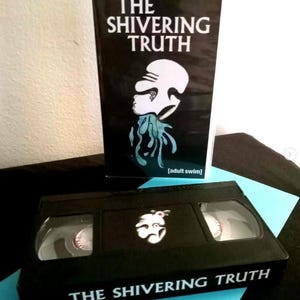 May include: Black VHS tape and book featuring the title "THE SHIVERING TRUTH" in white font. The book and tape have a graphic of a white face with blue tentacles. The Adult Swim logo is on the book.