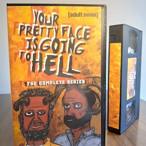 May include: A VHS tape of the Adult Swim show "Your Pretty Face Is Going to Hell." The cover features two cartoon devils with the show's title in orange and yellow text. The complete series is displayed on the cover.