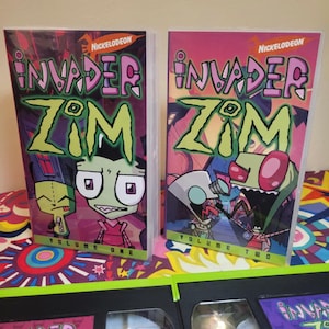 May include: Two Invader Zim VHS tapes and two DVD cases are displayed. The DVD cases are labeled "Volume One" and "Volume Two" with the Nickelodeon logo. The tapes and cases feature the show's title and characters in vibrant colors.