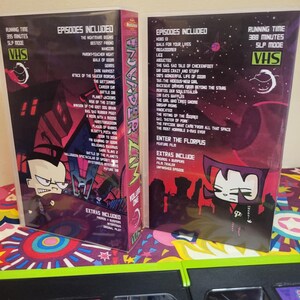 May include: Two VHS tapes of the animated series Invader Zim. The tapes are in their original packaging, featuring character art and episode lists. The tapes are labeled Volume One and have a running time of 395 and 388 minutes.