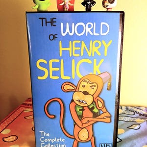 May include: A VHS tape titled "The World of Henry Selick" with a cartoon monkey illustration. The tape is blue with yellow text and has small character figurines on top. The complete collection is written on the bottom of the tape.