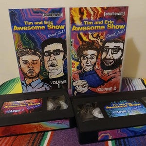 May include: Two VHS tapes and their covers for "Tim and Eric Awesome Show, Great Job!" Volume 1 features two men, and Volume 2 features two different men. The covers have the Adult Swim logo. The tapes are black.