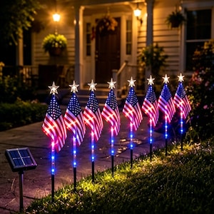 May include: A row of eight solar-powered garden lights, each featuring a miniature American flag topped with a glowing white star. The flag poles are illuminated with blue LED lights, and a separate black solar panel unit is positioned nearby.