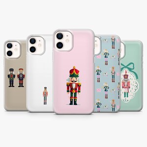 Puede incluir: Cinco fundas para smartphone con diseños de cascanueces. Las fundas incluyen una beige con dos cascanueces, una transparente con un solo cascanueces, una rosa con un cascanueces grande, una azul con un patrón y una verde con un lazo.