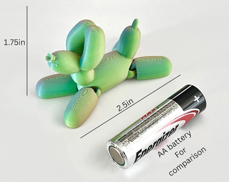 May include: A green and blue 3D-printed balloon dog, 2.5 inches long and 1.75 inches tall, with articulated joints. An AA battery is included for size comparison. The dog is made of layered plastic and has a whimsical appearance.