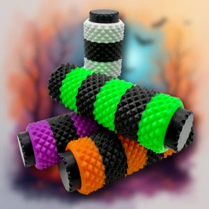 May include: A collection of colorful, textured handlebar grips. The grips feature a repeating diamond pattern and come in various color combinations, including green and black, purple and black, and orange and black. A matching white and black grip is also visible.