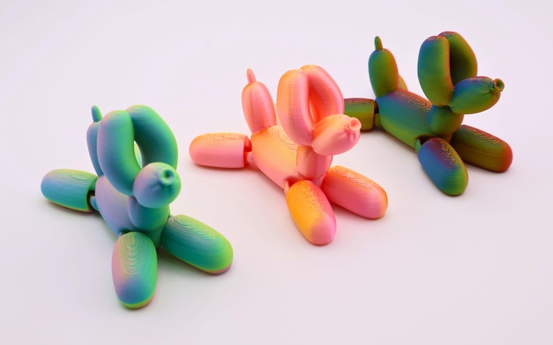 May include: Three colorful balloon dog sculptures in shades of pink, orange, green, and blue. The whimsical figures are posed in different positions, with one lying down and two standing. The dogs are on a white background.
