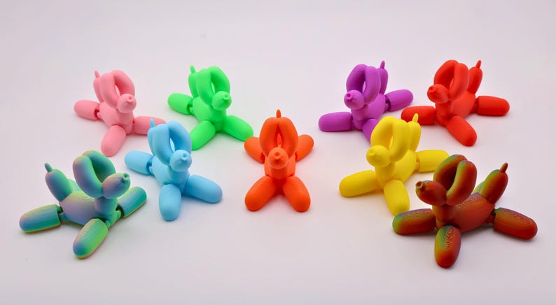 May include: A collection of colorful balloon dog figurines in various shades, including pink, green, blue, orange, purple, yellow, red, and a rainbow gradient. These playful sculptures are arranged on a white surface.