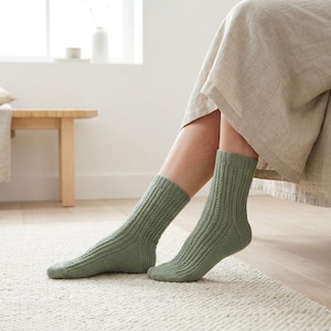 May include: A pair of sage green mid-calf socks featuring a vertical ribbed knit pattern. The socks are constructed with a reinforced heel and toe section, providing a textured appearance that extends from the cuff down to the foot area.