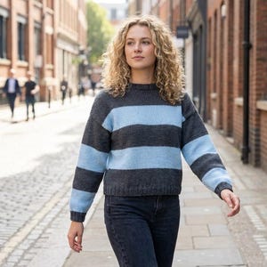 May include: A long-sleeve knit sweater featuring horizontal stripes in alternating dark charcoal gray and light baby blue. The sweater has a crew neckline, ribbed cuffs, and a ribbed hem, paired with dark denim jeans.