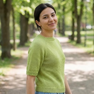 May include: A lime green short-sleeved knitted sweater featuring a ribbed crew neckline, ribbed sleeve cuffs, and a ribbed hem. The garment is constructed with a stockinette stitch pattern and raglan sleeves, providing a simple and clean design.