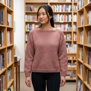 May include: A dusty rose long-sleeved jumper featuring a wide boat neckline and raglan sleeves. The garment is constructed with a smooth knit texture, ribbed cuffs, and a ribbed hemline, providing a clean and simple silhouette for everyday wear.