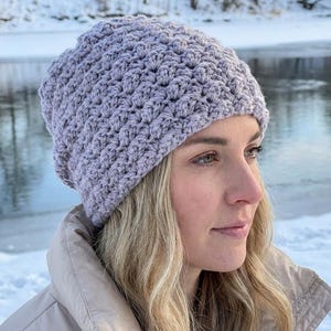 May include: A light lavender crochet beanie featuring a textured bobble stitch pattern. The hat has a rounded crown and a snug fit, crafted from yarn with a consistent knit structure throughout the entire surface of the headwear accessory.