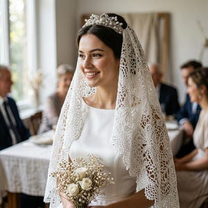 May include: A white lace veil with intricate floral patterns draped over the head, paired with a silver-toned tiara featuring embedded white pearls and clear crystals. The veil is worn over a smooth, solid white sleeveless garment.