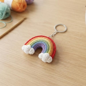 Peut inclure: Un porte-clés arc-en-ciel crocheté composé d'un arc multicolore en fil rouge, orange, jaune, vert, bleu et violet. L'arc-en-ciel présente un petit nuage blanc crocheté à chaque extrémité et est relié à un anneau brisé en métal argenté.