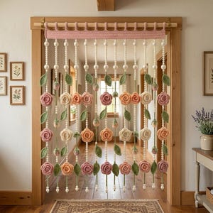 May include: A decorative doorway curtain featuring multiple vertical strands of white beads interspersed with crocheted pink, peach, and cream-coloured roses and green leaves. The strands hang from a wide, pink crocheted valance on a wooden rod.