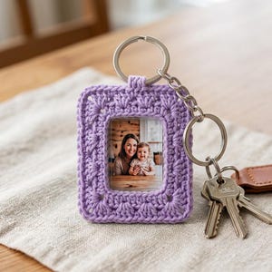 May include: A rectangular lavender crochet frame keychain featuring a central clear window displaying a photograph of an adult and a child. The frame is attached to a silver-toned metal split ring and chain, which holds a set of metal keys.