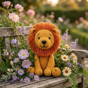 Puede incluir: Un león de peluche tejido a ganchillo con un cuerpo amarillo dorado y una melena naranja gruesa y texturizada. El león tiene ojos y nariz negros bordados, sentado erguido con las patas delanteras descansando sobre su regazo.