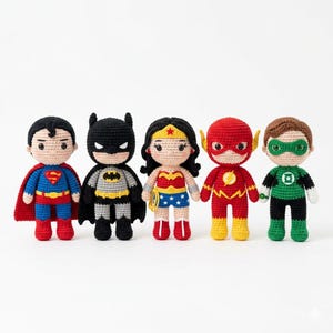 Op de afbeelding: Een set van vijf gehaakte poppen die superhelden voorstellen. De figuren zijn Superman in blauw en rood, Batman in zwart en grijs, Wonder Woman in rood en blauw, The Flash in rood en geel, en Green Lantern in groen en zwart.