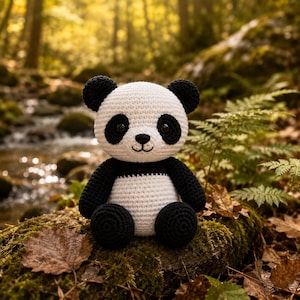 Op de afbeelding: Een handgemaakt gehaakt panda-speeltje met een witte kop en romp, voorzien van zwarte oren, oogvlekken, armen en benen. De panda heeft een geborduurde zwarte neus en mond, met donkere, ronde veiligheidsogen en een textuur van garen.