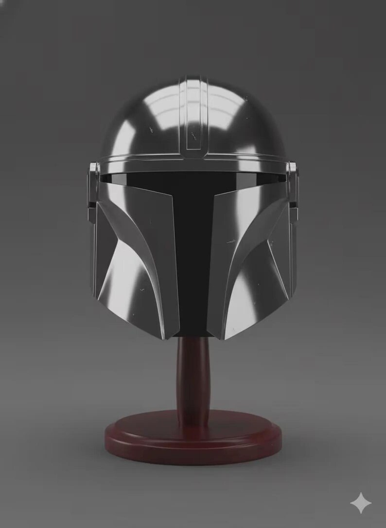 May include: A polished silver-coloured helmet with a smooth, rounded dome and a distinct T-shaped black visor section. The helmet features a central ridge and angular cheek plates, mounted on a dark reddish-brown circular wooden display stand.