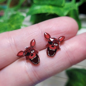 May include: A pair of red and white cartoon character earrings. The character has a black eye patch and a wide open mouth. The earrings are made of resin and are about 1 inch in diameter.