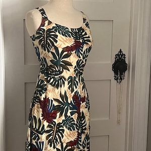 May include: A sleeveless dress with a white background and a tropical leaf print in shades of green, brown, red, and blue.