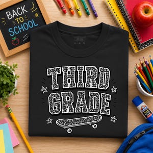 May include: A black t-shirt featuring the white text "THIRD GRADE" in a varsity-style font with a speckled texture. Below the text is a graphic of a skateboard with the same speckled pattern, surrounded by four small white star icons.