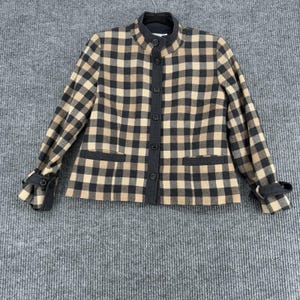 May include: A tan, black, and gray plaid jacket with a mandarin collar and button-up front. The jacket has long sleeves with buttoned cuffs and two small pockets. The trim and buttons are dark gray.