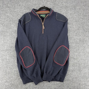 May include: A navy blue quarter-zip pullover sweater featuring dark navy shoulder patches and matching elbow patches outlined in red piping. The collar interior has a multi-coloured striped pattern, and the brand name Orvis is printed on the inner neck label.