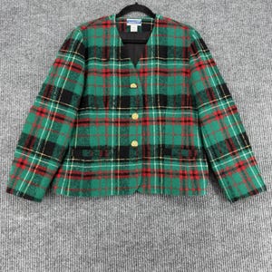 Puede incluir: Un blazer a cuadros verdes, rojos, negros y blancos con botones dorados. El blazer tiene cuello en V y dos bolsillos delanteros. La chaqueta está colgada de una percha negra.