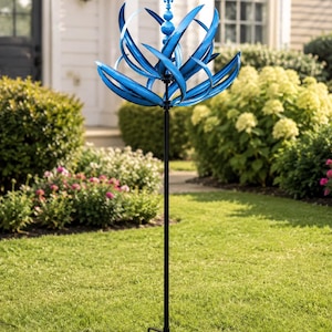 Puede incluir: Un molinillo de viento de metal azul con aspas curvas en forma de pétalos dispuestas en una esfera, rematado con un remate decorativo. El molinillo está montado sobre un poste de metal negro con una base de cuatro puntas para estabilidad.