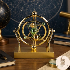 May include: A gold-toned kinetic sculpture featuring a central green sphere surrounded by rotating rings and smaller metallic spheres. The structure is mounted on a rectangular gold base, designed to mimic the appearance of a planetary model.