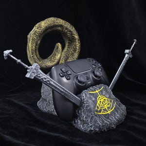 Könnte beinhalten: Ein schwarzer Videospiel-Controller ruht auf einem grauen, felsartig texturierten Ständer mit einem gelben kreisförmigen Symbol. Der Ständer wird von zwei silberfarbenen Schwertern flankiert und von einem gebogenen, goldfarbenen Ring gekrönt.