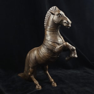 May include: A dark brown, sculpted horse figurine in a rearing pose. The sculpture features a distinct layered or banded texture across its neck and body, with a defined mane and tail. The horse is depicted with its front legs lifted off the ground.