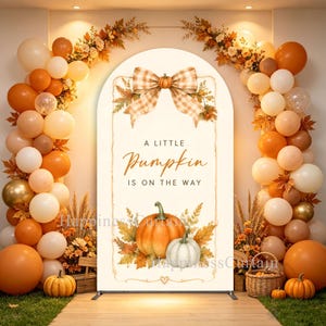 May include: An arched backdrop featuring a beige and white checkered bow, autumn leaves, and two pumpkins with the text A LITTLE Pumpkin IS ON THE WAY. The display is framed by a dense arrangement of orange, white, and gold balloons and foliage.